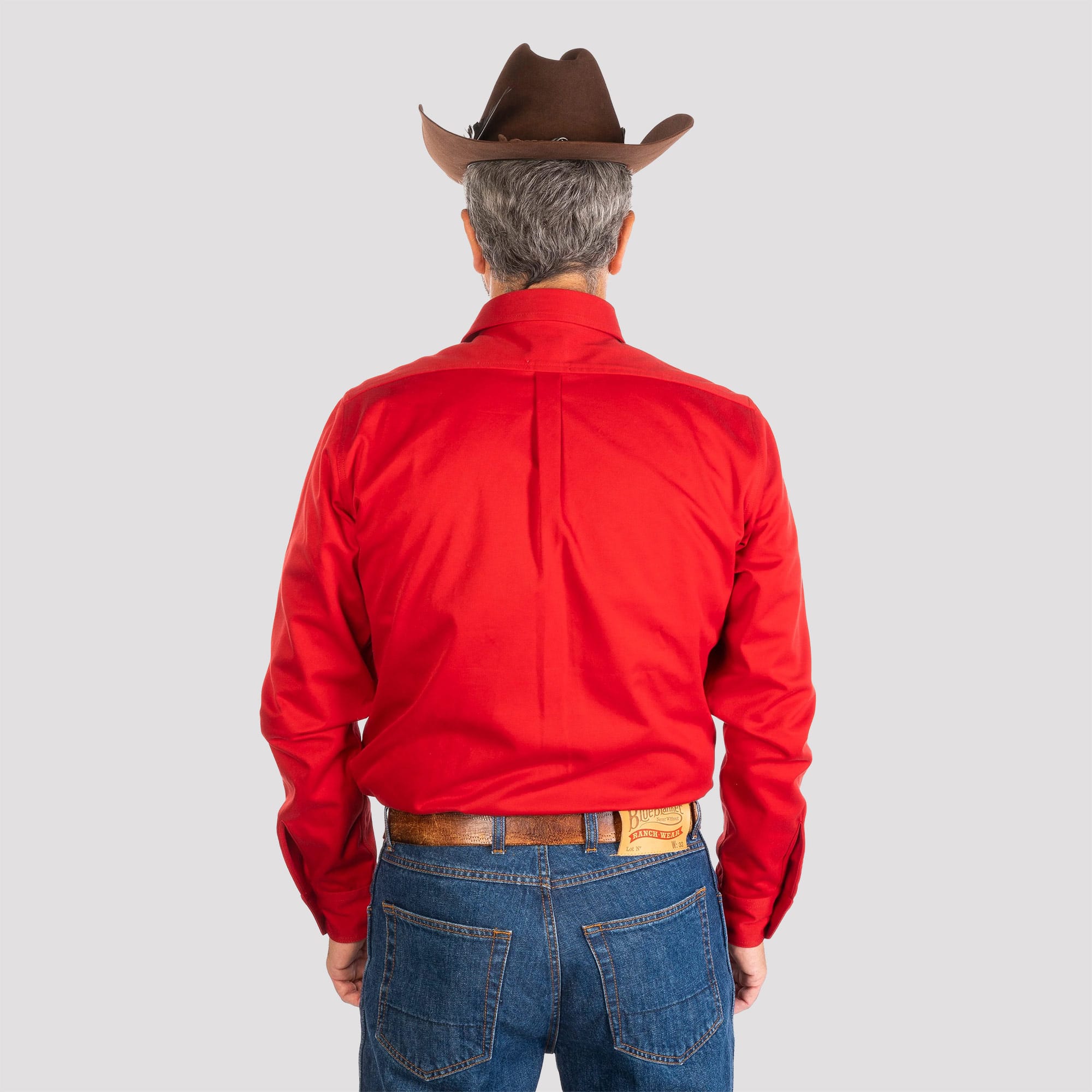 Person wearing a red shirt, blue jeans, and a brown cowboy hat on a gray background
